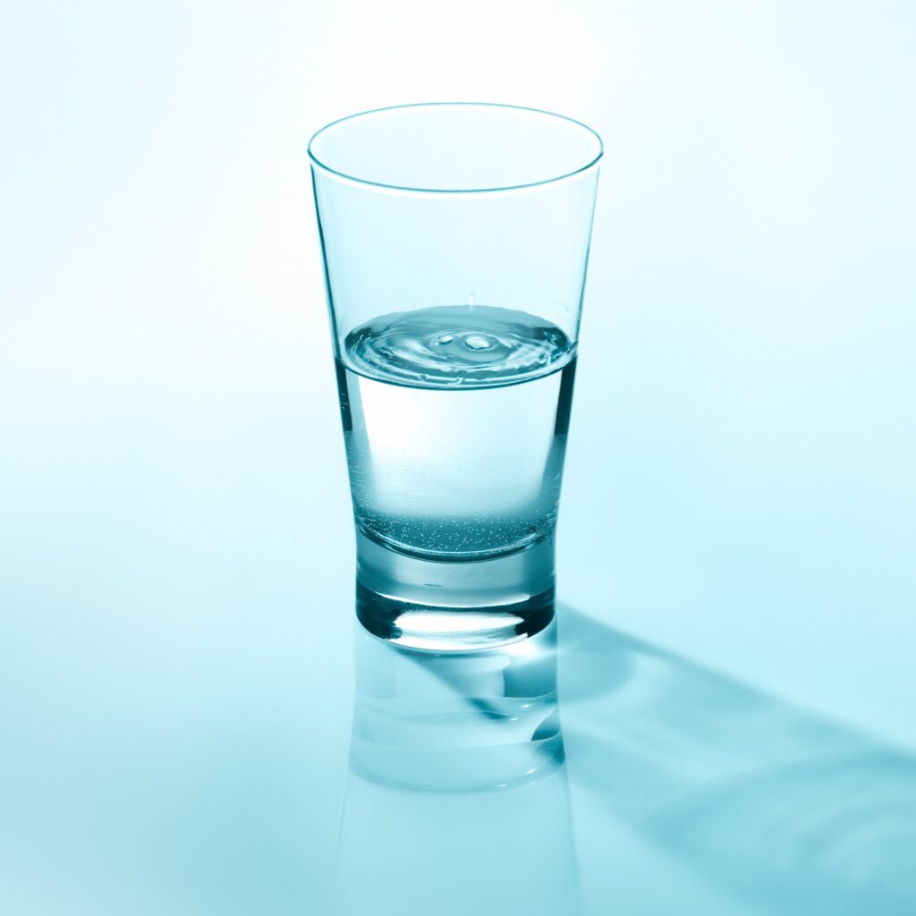 A glass of drinking water on a blue background with a shadow reflection.